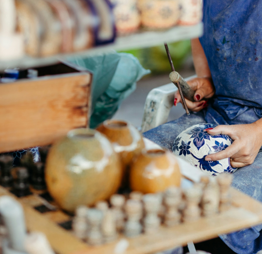 An artisan carving intricate blue floral patterns into a ceramic bowl at a workbench representing the Artisan Home and Living collection.